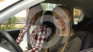 Happy female smiling into camera, sitting in car with instructor, driving school