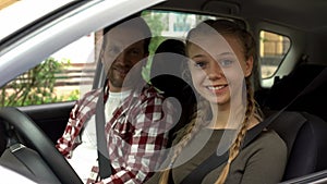 Happy female smiling into camera, sitting in car with instructor, driving school