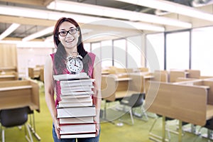 Happy female student bring stack of books and clock