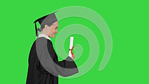 Happy female student in graduation robe walking and cheering with her diploma on a Green Screen, Chroma Key.