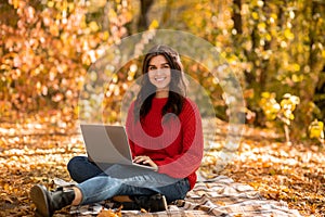 Happy female student learning online, doing her homework on laptop computer at autumn park