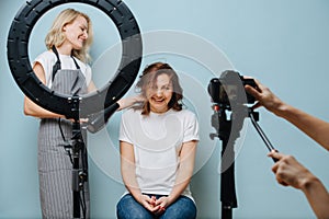 Happy female stylist drying client`s brown hair while photo is taken