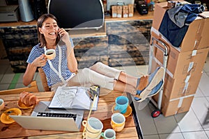 Happy female talking on her cell phone and drinking coffee with her legs on the table. casual, relaxed, break, pause