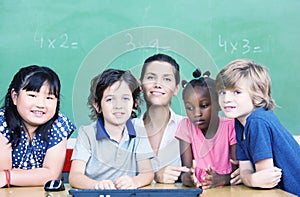 Happy female teacher with her multirace classroom at school desk