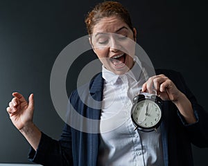 Happy female teacher in a pantsuit looks at the alarm clock while standing at the blackboard. A woman rejoices at the