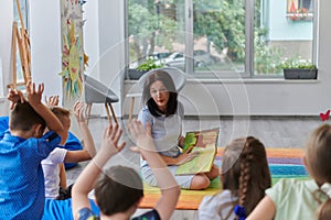 A happy female teacher sitting and playing hand games with a group of little schoolchildren