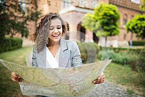 Happy female tourist with backpack on shoulders exploring map while standing in alley near vintage building, trendy woman traveler