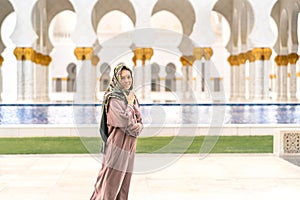 Happy female tourist wearing scarf and dress in The Sheikh Zayed Grand Mosque in Abu Dhabi.