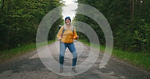 Happy female traveler dancing funny and fun. A woman in a yellow sweater and hat with a backpack on the road in the