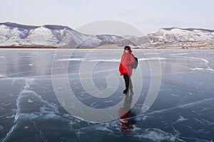 A happy female traveler in a red down jacket stands on the transparent ice