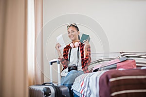 happy female traveler showing ticket and passport sitting on bed