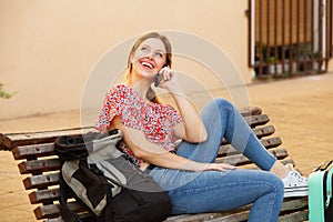 Happy female traveler sitting with bags and talking on cell phone