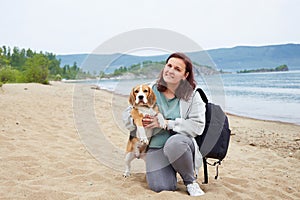 A happy female traveler is sitting on a sandy beach in an embrace with her dog