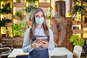 Happy female waitress using digital tablet while wearing protective face mask at the restaurant or cafe. Open again after lock