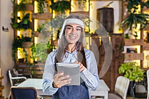 Happy female waitress using digital tablet while wearing visor at the restaurant or cafe. Open again after lock down due to