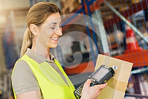 Happy female Worker with barcode scanner, scans bar-code of package, standing at warehouse