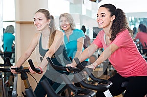 Happy females of different age training on exercise bikes