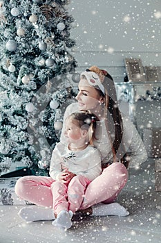 Happy festive mother and daughter hugging sitting together at decorating beautiful Christmas tree