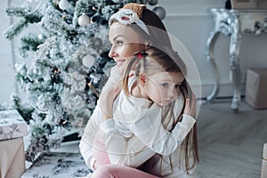 Happy festive mother and daughter hugging sitting together at decorating beautiful Christmas tree