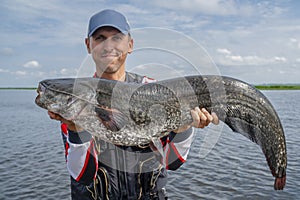 Happy fisherman with big catfish fish trophy at the boat with fishing tackles