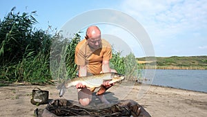 Happy fisherman with big fish trophy in hands. Success carp fishing. Angler on the river bank