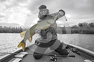 Happy fisherman with big pike fish trophy at the boat with fishing tackles