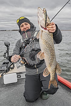 Happy fisherman with big pike fish trophy at the boat with fishing tackles