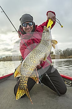 Happy fisherman with big pike fish trophy at the boat with fishing tackles photo
