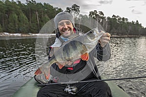 Happy fisherman hold big perch fish at boat with tackle. Success fishing at wild lake