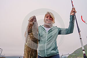 Happy Fisherwoman holding big arctic cod. Norway happy fishing. Woman with cod fish in hands