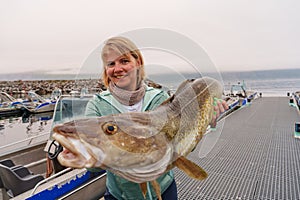 Happy Fisherwoman holding big arctic cod. Norway happy fishing. Woman with cod fish in hands