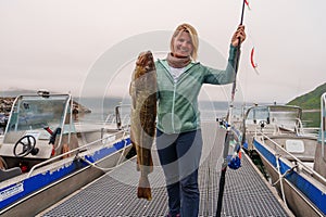 Happy Fisherwoman holding big arctic cod. Norway happy fishing. Woman with cod fish in hands