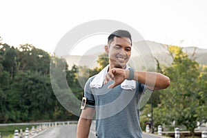 A happy, fit Asian man is checking his calories burning on his smartwatch after running in a park