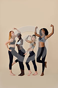 Happy fit diverse young women group showing muscles. Vertical full body.