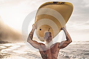 Happy fit senior having fun surfing at sunset time - Sporty bearded man training with surfboard on the beach