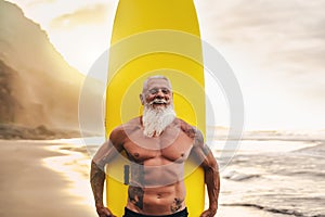 Happy fit senior having fun surfing at sunset time - Sporty bearded man training with surfboard on the beach