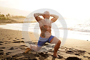 Happy fit senior man exercising on the beach during sunset time. In a healthy body healthy mind