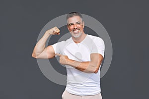 Happy fit sporty older man personal trainer showing biceps isolated on gray.