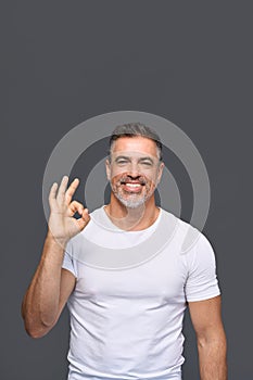 Happy fit sporty older man personal trainer showing ok isolated on gray.