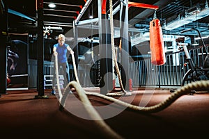 Happy fit woman with battle ropes exercise in the fitness gym