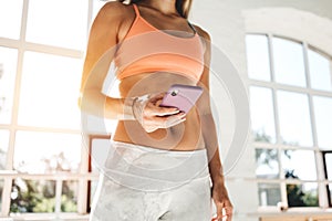 Happy fit woman counts calories and made post in blog after fitness workout. Healthy girl wearing sportwear hold smartphone in han