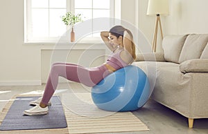 Happy fit young woman doing sit ups on exercise ball during fitness workout at home