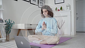 Happy fit young woman using laptop watching online yoga lesson at home.