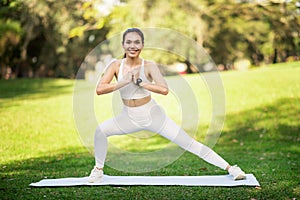 Happy fitness enthusiast performs a wide-legged squat on a yoga mat in a sunlit park