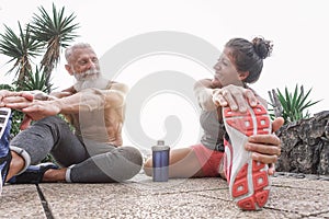 Happy fitness friends doing legs stretching exercises together in outdoor area