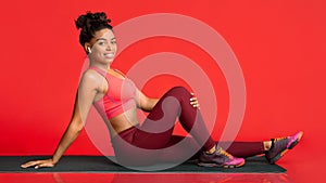 Happy fitness girl posing on yoga mat over red background