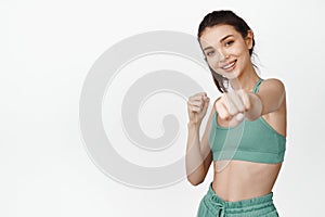 Happy fitness girl pucnhing, smiling and doing workout, goxing exercises with stretched out clenched fist, standing in