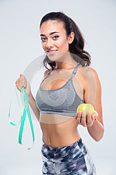 Happy fitness woman holding apple and measuring typ