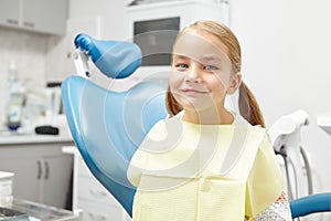 Happy five year old child sitting in the dentist`s office and smiling. Beautiful girl in the chair.