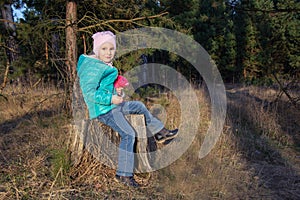 happy five-year-old girl sitting in a jacket on a stump in the woods in the spring